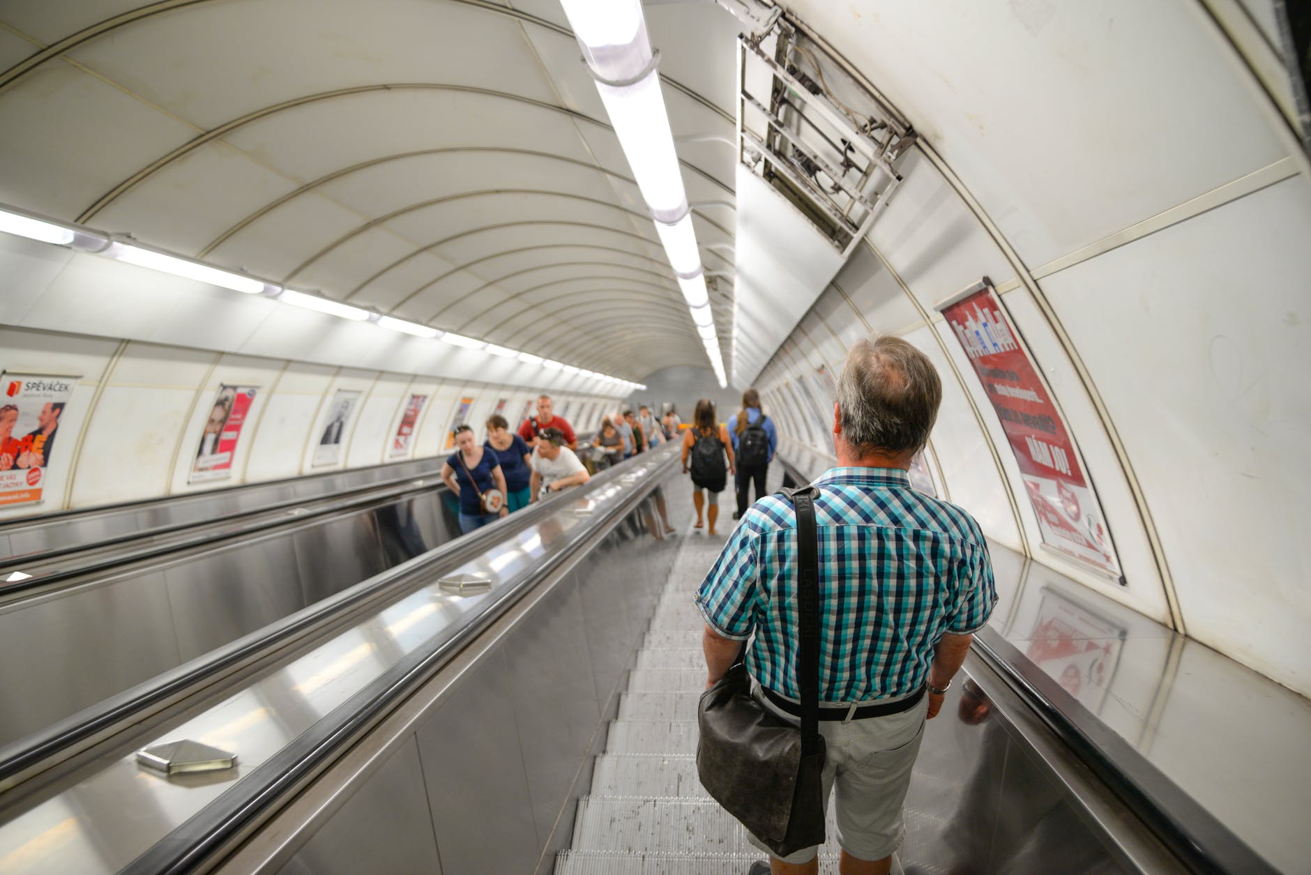 man wearing blue plaid shirt standing on subway escalator