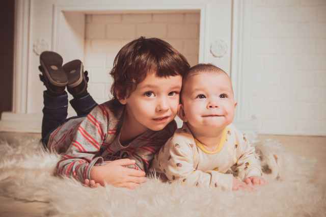 boy lying beside baby on mat