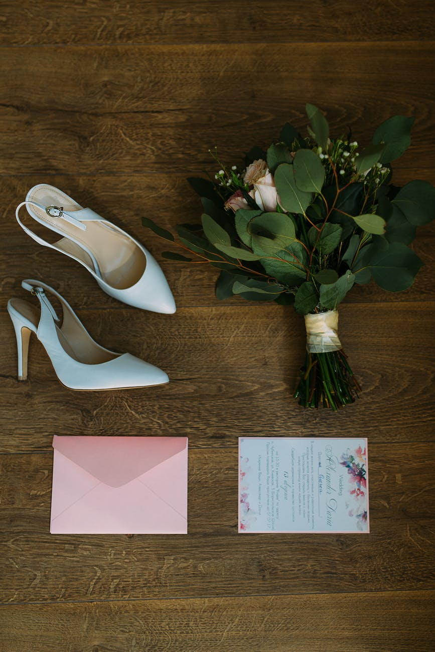 pair of white leather pointed toe slingback shoes beside bouquet of flowers
