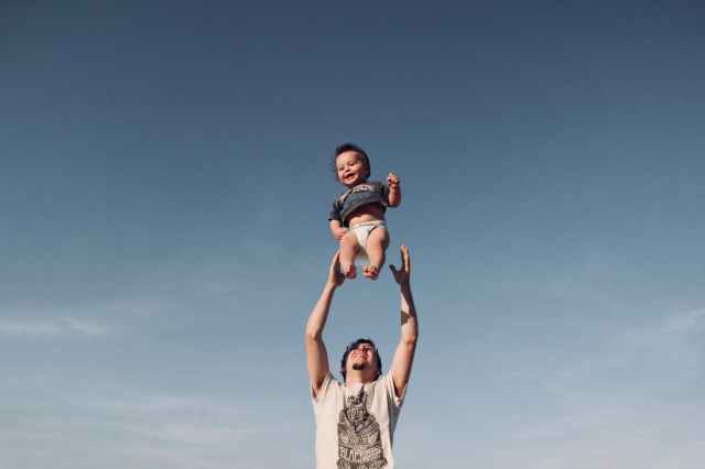 photo of man in raising baby under blue sky