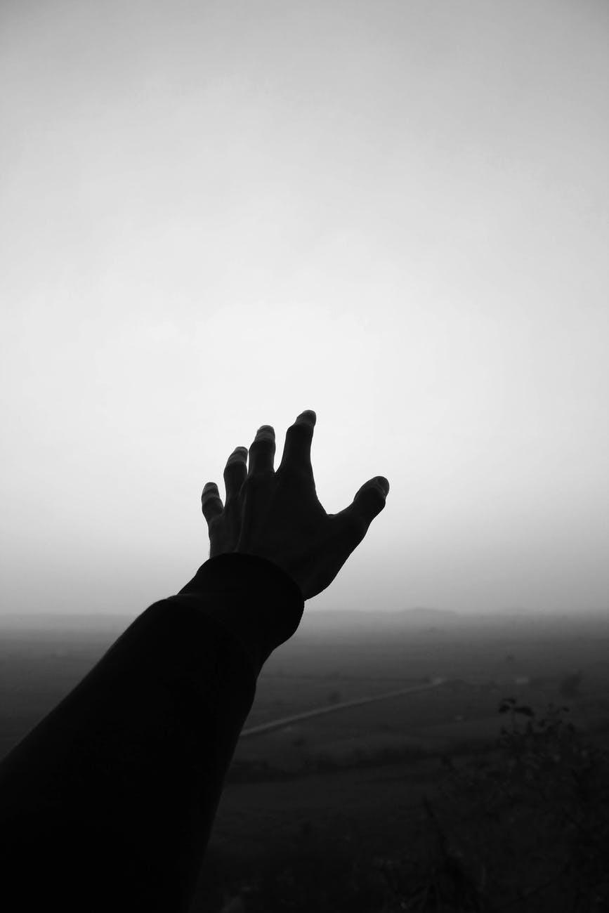grayscale photo of person s hand reaching for the sky
