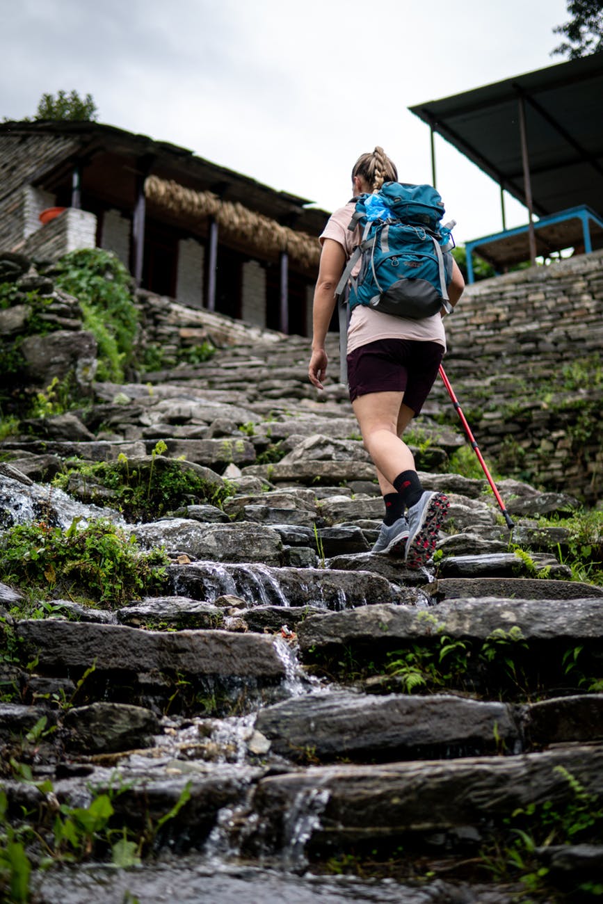 woman carrying black and blue backpack walking on rocky stairs